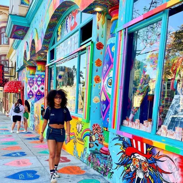 Donna che cammina lungo Haight Street con un murale colorato sullo sfondo.